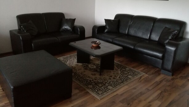 A living room with a black leather sofa, a matching ottoman, and a coffee table. There are two framed artworks on the wall.