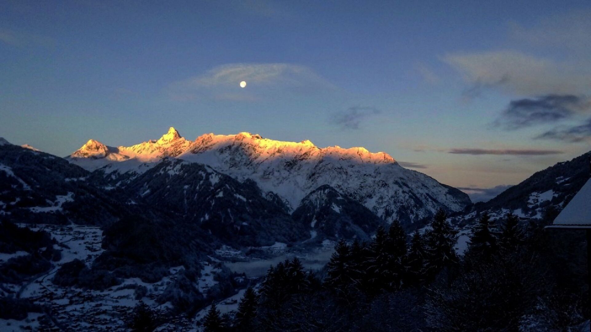 A mountain landscape with snow-covered peaks and a visible moon in the sky.