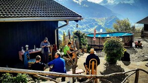 A rustic outdoor setting with a pool, wooden furniture, and a mountainous backdrop.
