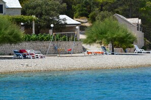 Une plage de galets avec des chaises longues et une balançoire.
