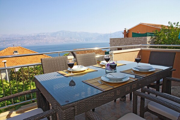 Une table à manger dressée avec des assiettes, des verres et des couverts, placée sur un balcon offrant une vue panoramique.