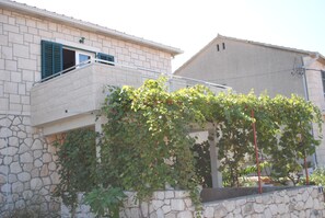 Un bâtiment à la façade en pierre, doté d’un balcon aux volets verts et d’un mur recouvert de vigne.