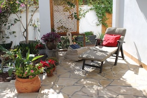 A patio area with a stone floor, a wicker chair with a red cushion, and various potted plants.