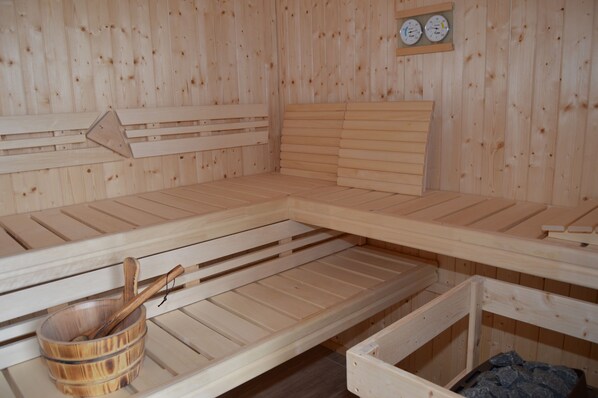 Una sala de sauna con bancos de madera, un balde de madera y un termómetro en la pared.