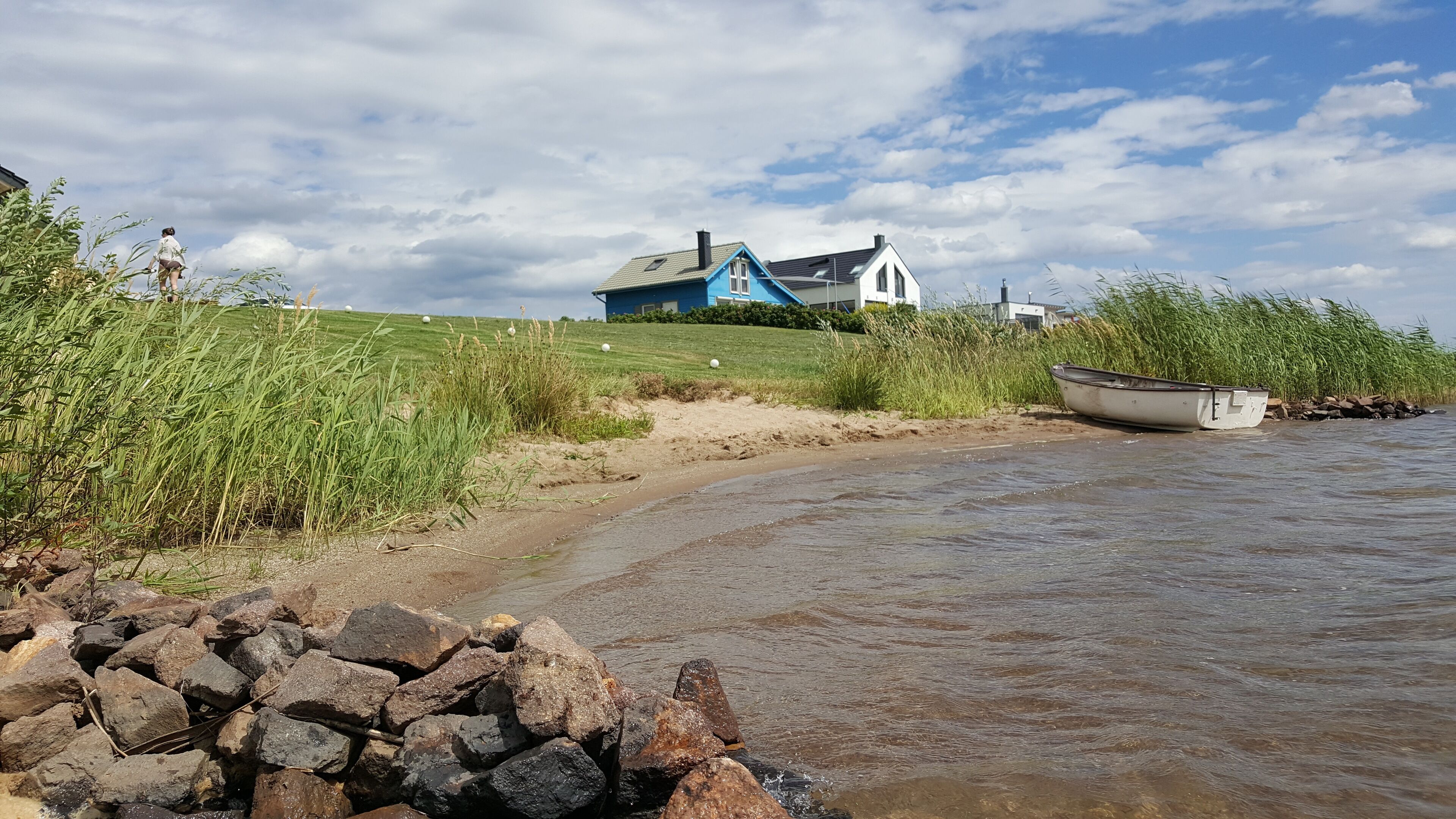 Een rivierzicht met een huis, een boot en een persoon die aan het water staat.
