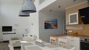 Una cocina moderna con horno empotrado, zona de comedor con mesa y sillas, un sofá y un televisor montado en la pared.