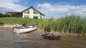 Una casa con un ventanal grande y una antena parabólica, un bote en la orilla y un área con césped.