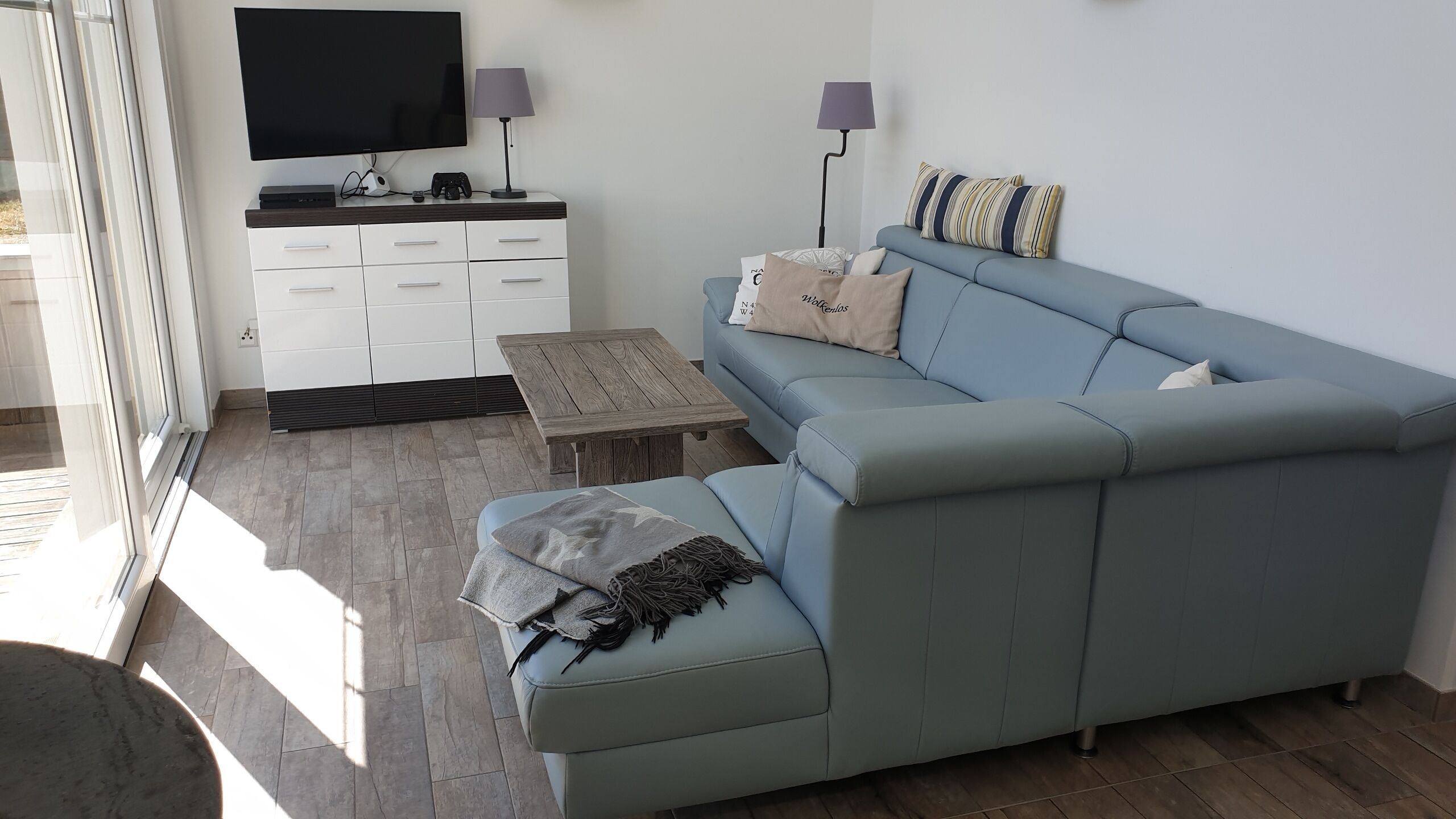 A modern living room with a light blue sofa, a wooden coffee table, a flat-screen TV, and a white cabinet.