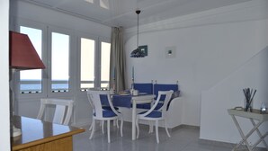 A dining area with a table and chairs, a view of the sea through large windows, and a ceiling light fixture. - Apartment directly on the sea with a fantastic view in Punta del Hidalgo (La Laguna / Punta del Hidalgo)