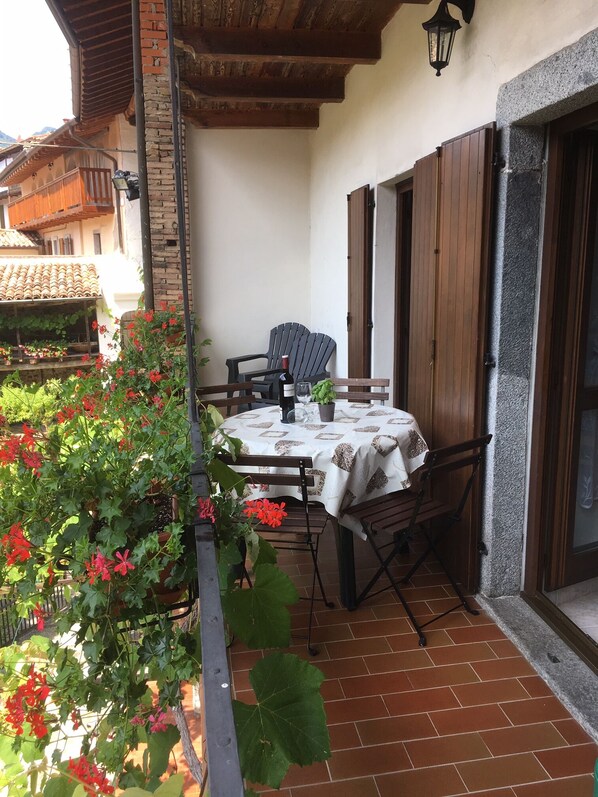 Eine Terrasse mit Tisch und Stühlen, umgeben von Kübelpflanzen und einem Pflasterboden.