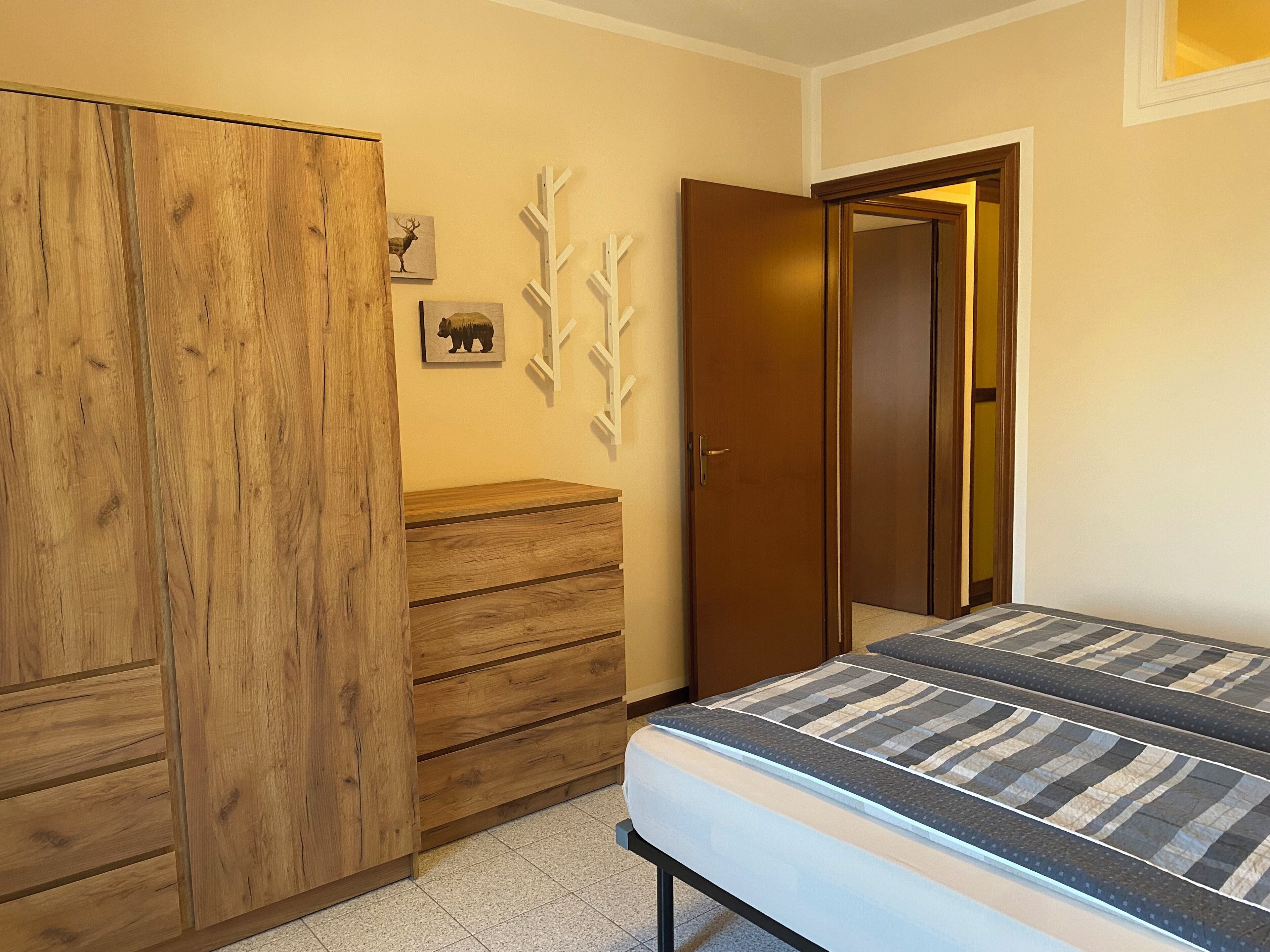 Un dormitorio con un armario de madera, una cama con ropa de cama a rayas y una puerta que da a otra habitación.
