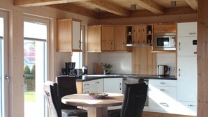 A kitchen with wooden cabinets, a microwave, and a sink. There is a dining table with chairs. - Luxurious solid-wood house with pool and sauna for 4 people in Allgäu (Aitrang)