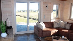 A cozy living room with a brown leather sofa, a coffee table, and a large sliding glass door leading to a patio. - Luxurious solid-wood house with pool and sauna for 4 people in Allgäu (Aitrang)