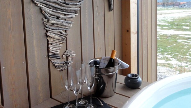 A wooden deck with a rustic wall art made of driftwood, a hot tub, and a view of a snowy landscape. - Luxurious solid-wood house with pool and sauna for 4 people in Allgäu (Aitrang)