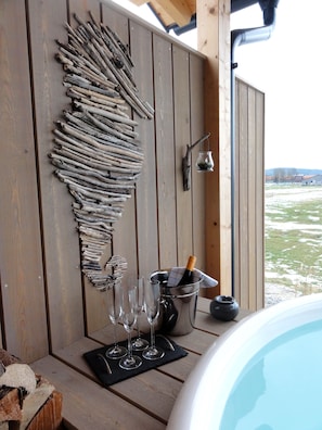 Une terrasse en bois agrémentée d’une décoration murale rustique faite de bois flotté, d’un jacuzzi et offrant une vue sur un paysage enneigé.