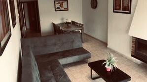 A living room with a sectional sofa, a dining table with chairs, a small black table with a plant, and a fireplace.