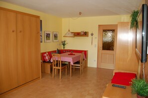 A compact living space with a dining area, a sofa, a TV, and a wooden wardrobe.