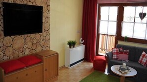A cozy living room with a stone wall, a flat-screen TV, a wooden cabinet, a red sofa, and a small table with a candle. - Apartment, 300m to the ski slope, everything on site, gr. Leisure offer winter + summer (Rußbach)