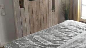 A bedroom with a wooden headboard, a flat-screen TV, a patterned bedspread, and a potted plant.