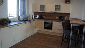 A modern kitchen with white cabinets, a microwave, an oven, and a sink. There is a window with a view of the outside, and a clock on the wall.
