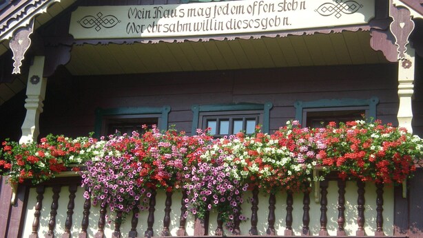 Una casa tradicional con un balcón decorado con flores de colores y un letrero en un idioma extranjero.