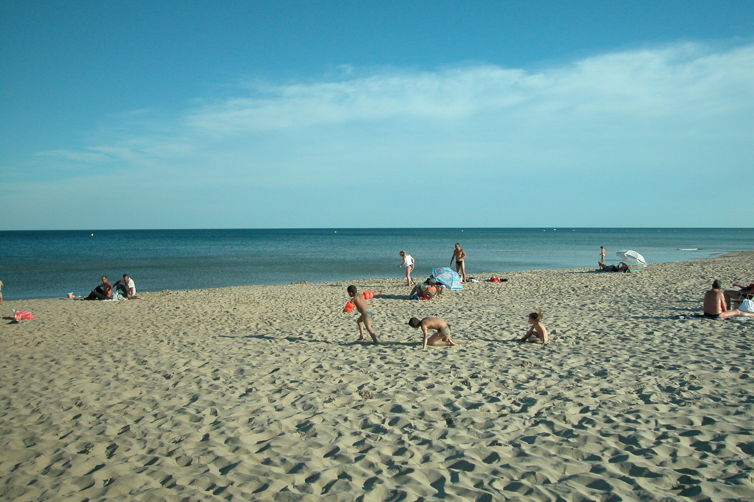 Een zandstrand met mensen die zonnebaden en spelen.