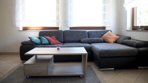 A modern living room with a sectional sofa, a coffee table, and large windows with sheer curtains. - Apartment Marion Altenkirch (Rüdesheim am Rhein)