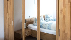 A bedroom with a wooden wardrobe, a bed with patterned bedding, and a small bedside table. - Apartment Marion Altenkirch (Rüdesheim am Rhein)