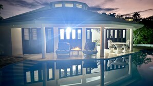 A modern house with a glass pool reflecting the sky. There are two chairs and a table by the pool. - Shell House a unique bungalow with 14m pool and sea view (Cabrera Maria Trinidad Sanchez)