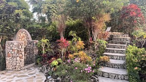 A stone staircase leading up to a stone archway surrounded by lush greenery and flowering plants. - Shell House a unique bungalow with 14m pool and sea view (Cabrera Maria Trinidad Sanchez)