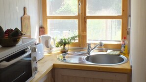 A compact kitchen with wooden cabinets, a built-in oven, a sink, and a window with a view of greenery outside.
