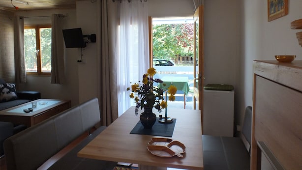 A cozy room with a wooden ceiling, a dining table with a vase of flowers, a sofa, and a television mounted on the wall.