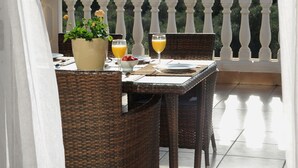 Un balcon agrémenté de meubles en osier, une table dressée pour deux personnes et une plante en pot.