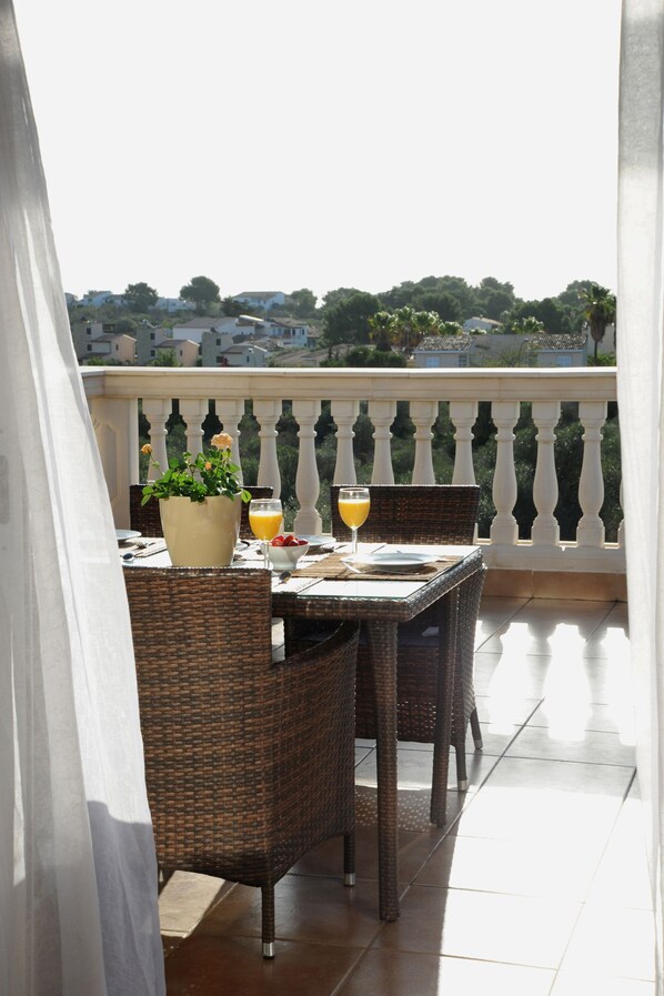 A balcony with wicker furniture, a table set for two, and a potted plant.