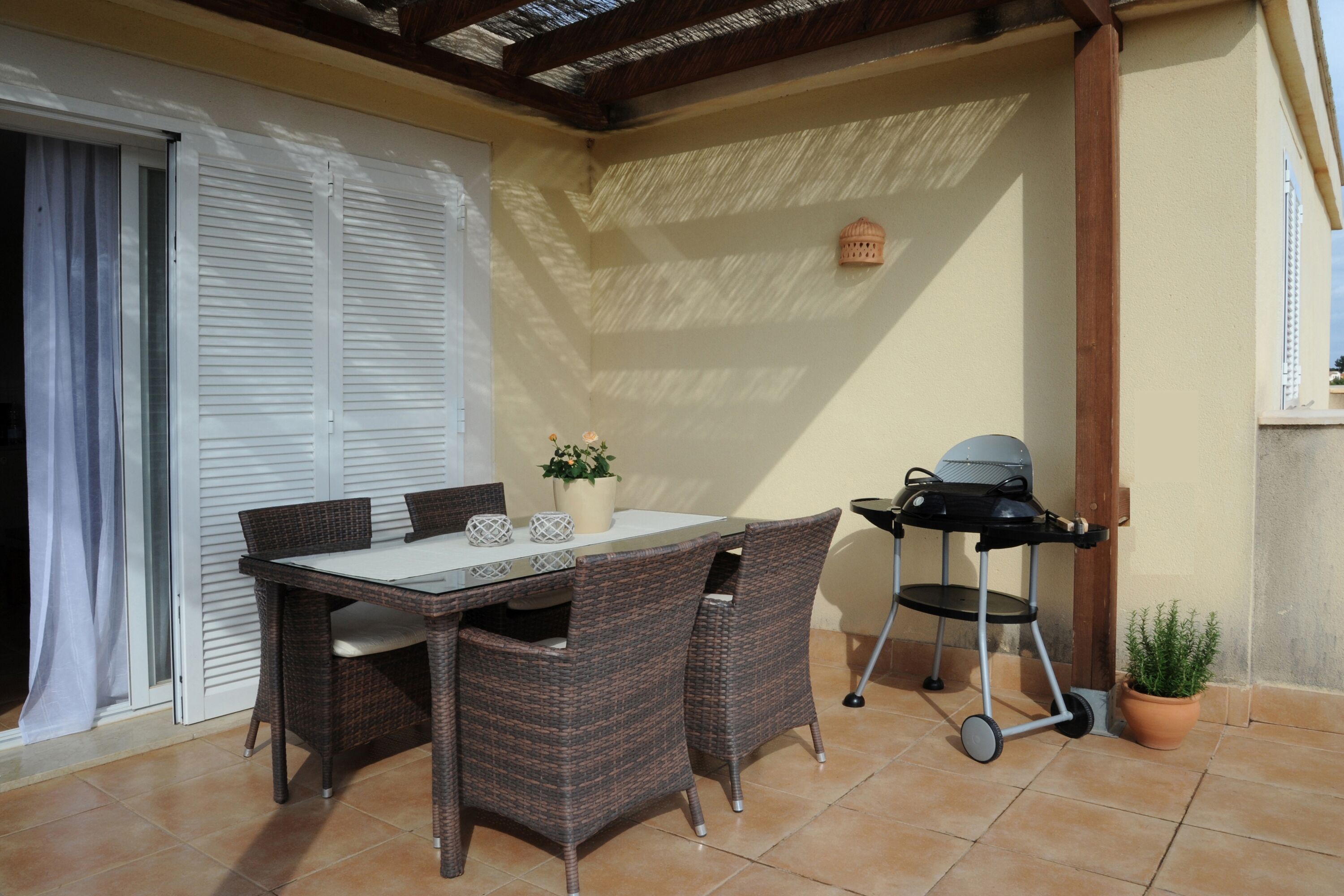 An outdoor patio with a table and chairs, a grill, and a potted plant.