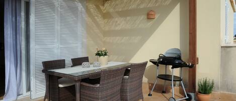 An outdoor patio with a table and chairs, a grill, and a potted plant.
