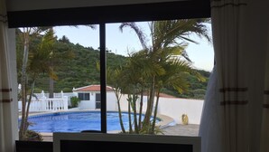 Blick auf einen Swimmingpool, umgeben von Palmen und einem weißen Gebäude mit rotem Dach.