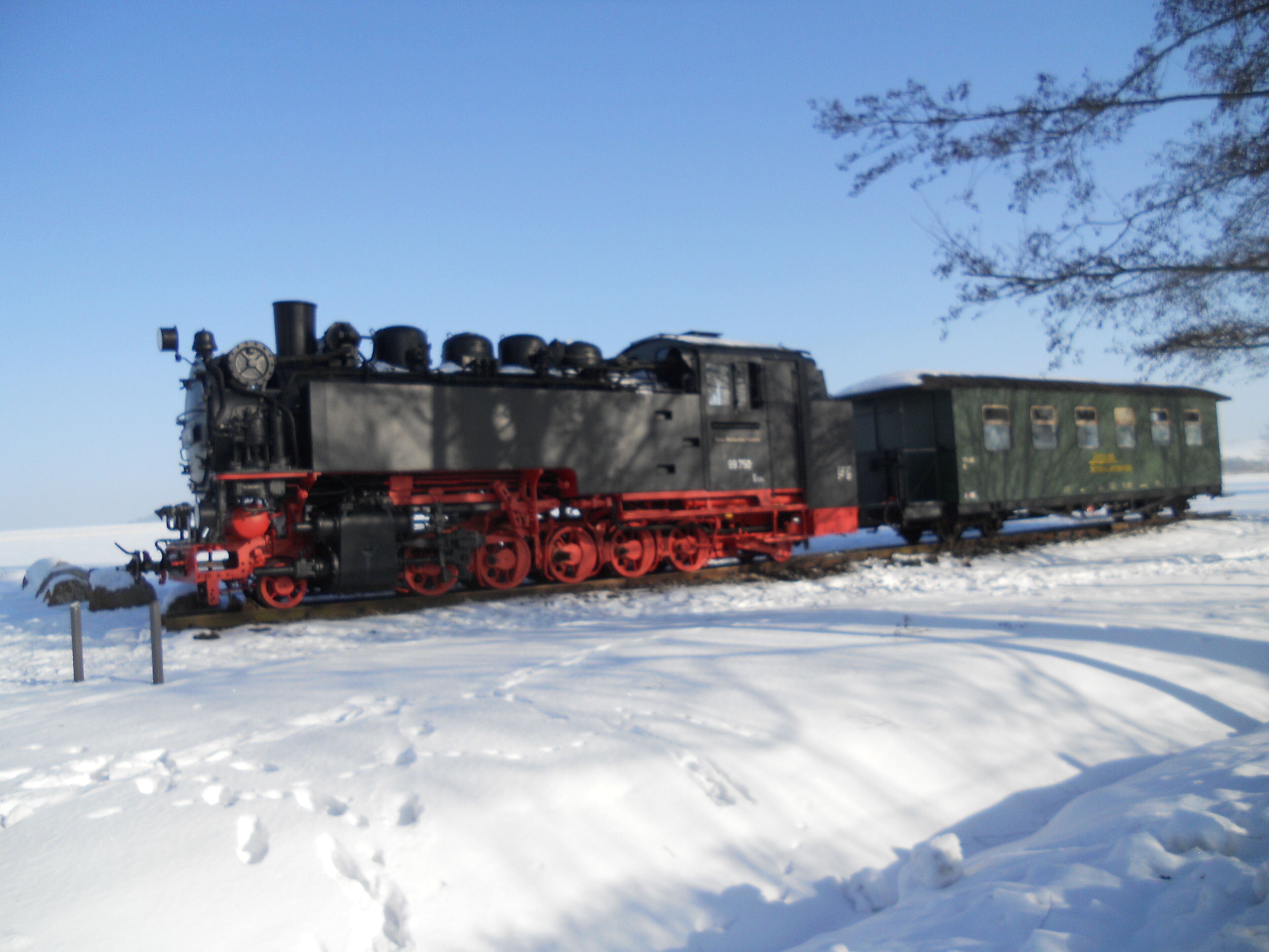 A steam locomotive with red wheels and a green caboose on a snow-covered track.