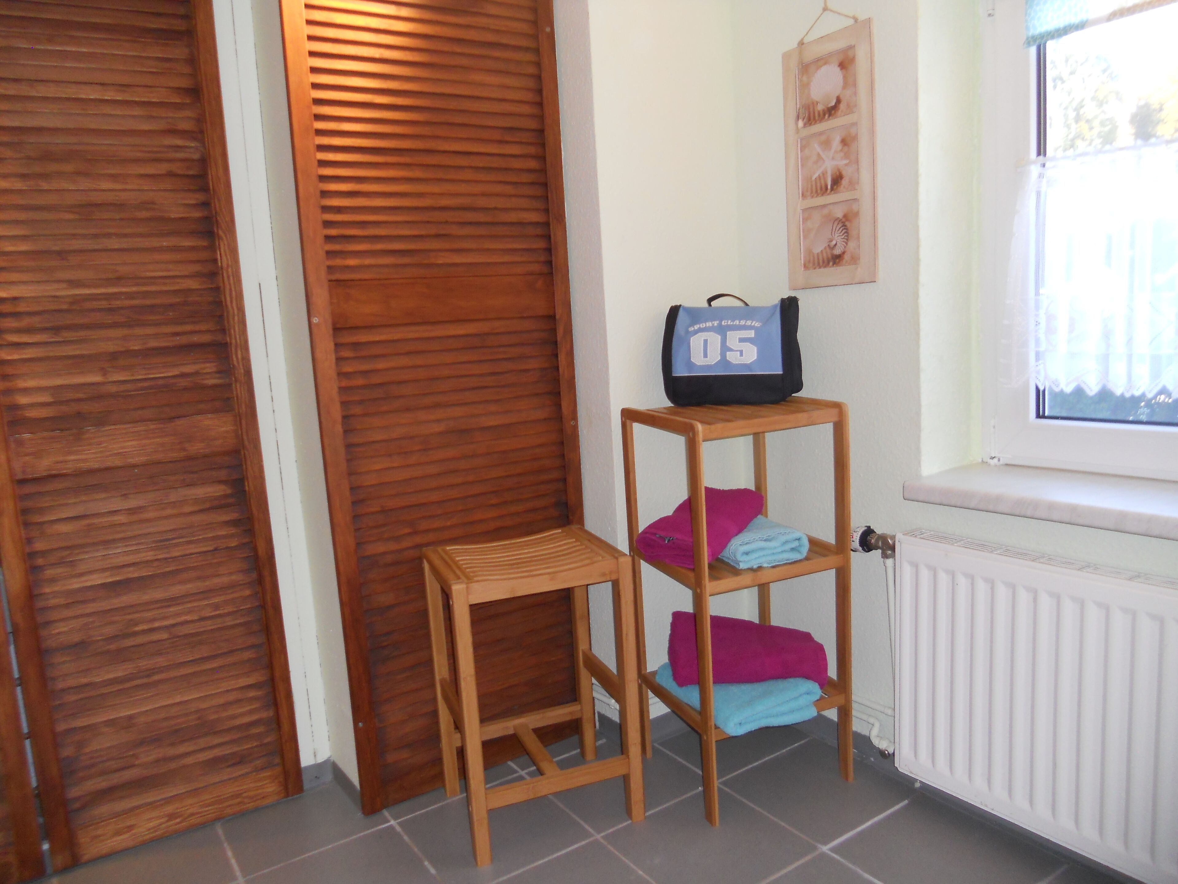 A room with a wooden door, a radiator, a window with a view, and a shelf with towels and a bag.