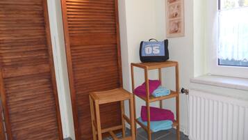 A room with a wooden door, a radiator, a window with a view, and a shelf with towels and a bag.