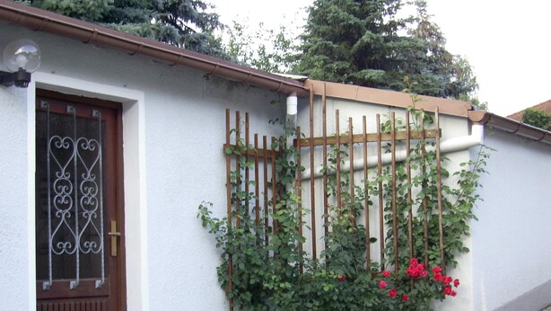 Una casa con fachada blanca, una puerta marrón y un pequeño jardín con flores rojas.