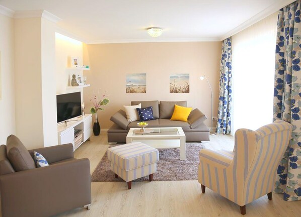 A living room with a sofa, armchair, ottoman, coffee table, TV, and artwork on the wall.