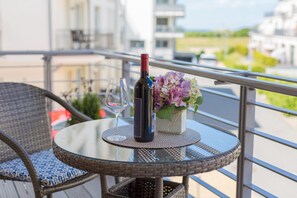 A round glass table with a wicker chair, a bottle of wine, two wine glasses, and a vase with flowers on a balcony.