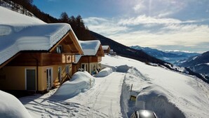 Un albergue cubierto de nieve con cabañas de madera, cielo despejado y vistas a montañas distantes.