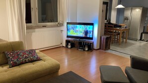 Un salon avec un téléviseur, un canapé et un pouf.
