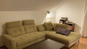 Un canapé modulable assorti d’un pouf, une table basse en bois et une lampe sur pied dans un salon doté d’un plancher en bois et de murs blancs.