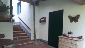 Un pasillo estrecho con una escalera de madera, una puerta verde y un aparador de madera con adornos.