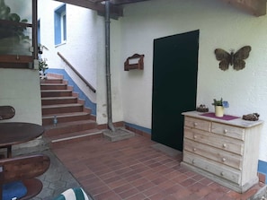 Un pasillo estrecho con una escalera de madera, una puerta verde y un aparador de madera con adornos.