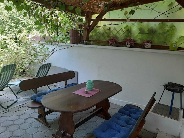 An outdoor patio with a wooden table and benches, surrounded by potted plants and a pergola. - ... The holiday destination Dingolfing-Landau - lovingly furnished with much comfort! (Landau a.d. Isar)