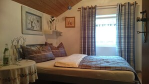 Un dormitorio con cama, mesita de noche, ventana con cortinas y adornos en la pared.